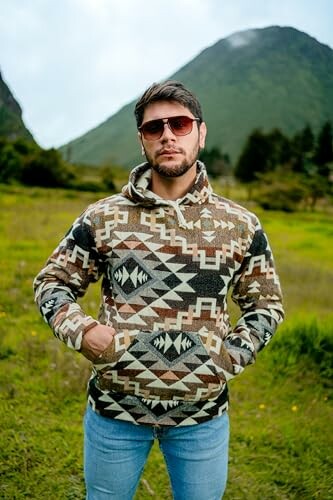 Man wearing a geometric patterned hoodie standing outdoors with mountains in the background.