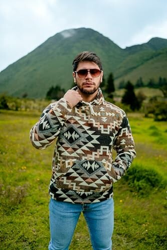 Man in patterned jacket standing in a field with a mountain in the background.