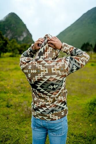 Person in patterned jacket adjusting hood in nature.