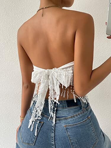 Person wearing a backless white lace top with jeans, showing a tied bow and fringe details.