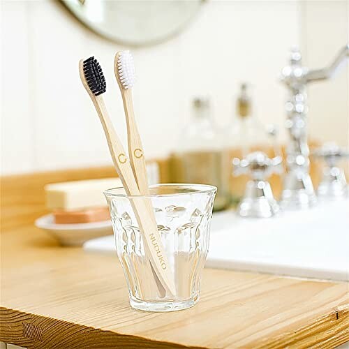 Two bamboo toothbrushes in a glass on a bathroom counter, highlighting the eco-friendly features.