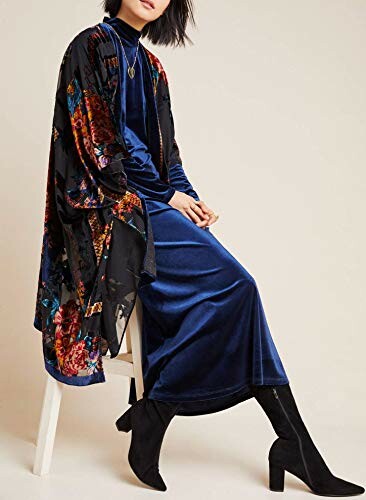 Person wearing a blue velvet dress with a floral kimono and black boots, seated on a stool.