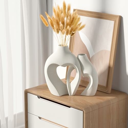 Modern ceramic vases with dried flowers on wooden dresser.
