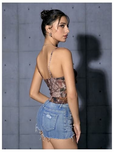 Woman in denim shorts and patterned top against concrete wall