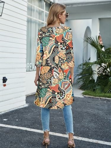 Woman wearing a colorful patterned dress and jeans standing outdoors.