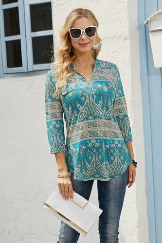 Woman in blue patterned top and sunglasses holding a clutch