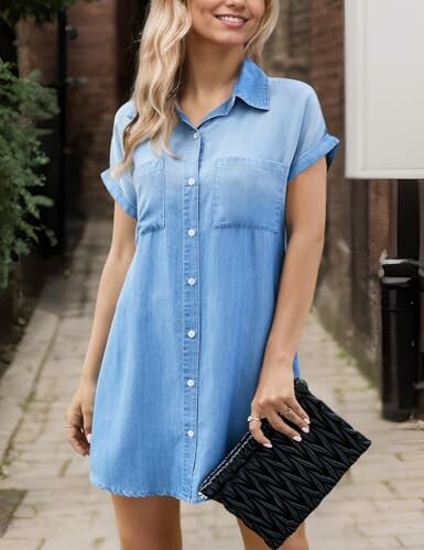 Woman in denim shirt dress holding a black clutch.